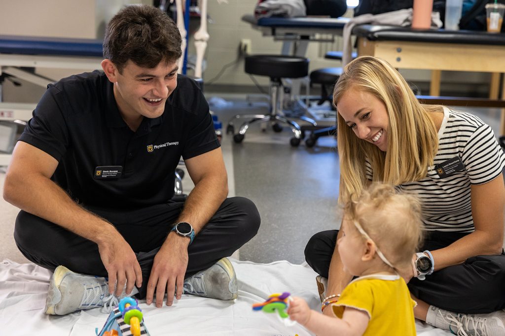 Two individuals smiling while looking at a baby.